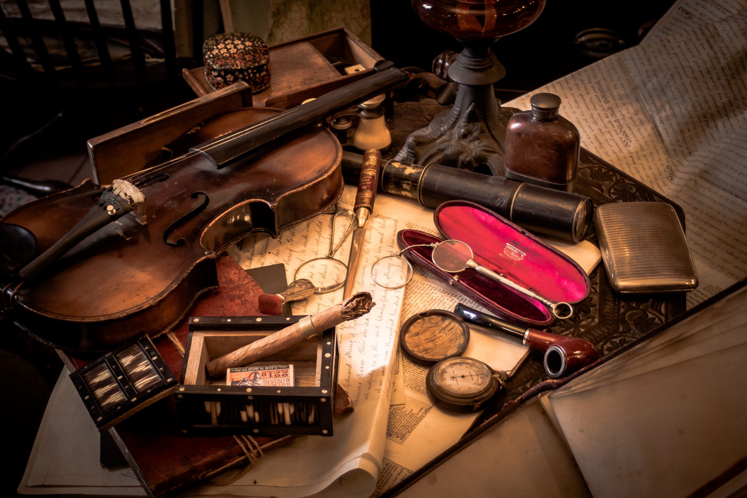Mesa victoriana con un violín, lupa, pipa, manuscritos y objetos de investigación inspirados en Sherlock Holmes.